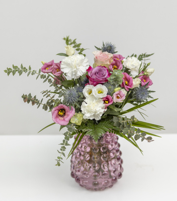 Bouquet delicato sulle tonalità del rosa e del bianco inserito in un bellissimo vaso di vetro color rosa antico. Nel bouquet sono stati inseriti: rose, garofani, eryngium e molti dettagli verdi