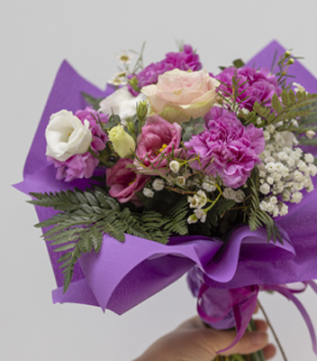 Bouquet sulle tonalità del viola composto da: rose, garofani, velo di sposa e felce. Il bouquet è avvolto in una carta viola che ne esalta i fiori, in basso si scorge una mano che sorregge il bouquet