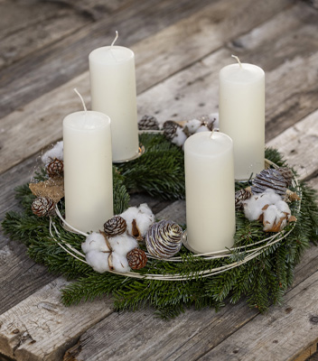 Corona d'avvento composta da quattro candele bianche, decorata con rami di abete, pigne e fiori di cotone sui toni del bianco e marrone