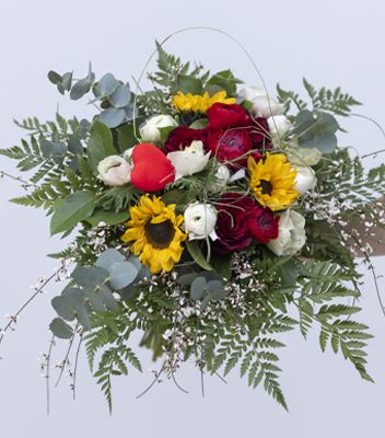 Bouquet di fiori colorati con rose rosse, girasoli, ranuncoli bianchi e rossi, anemoni e foglie verdi su sfondo chiaro