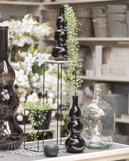 intro_decorCasa Composizione decorativa con vasi in vetro scuro, dettagli di verde artificiale e accessori per interni, perfetta per arredare con eleganza.